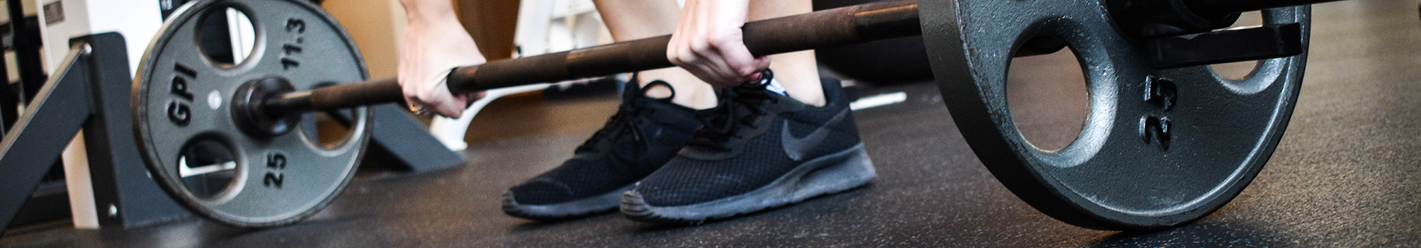 The shoes of a student is shown on the Fitness Center floor between the weights on a dumbbell before it is lifted off the floor. 