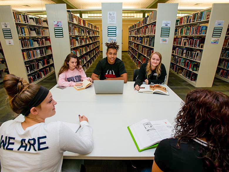 5 students talking at a table in the library