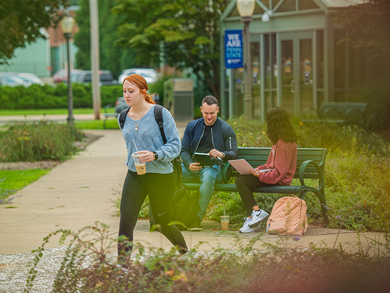 Penn State Shenango campus pedestrian mall with two students on bench and another walking to class