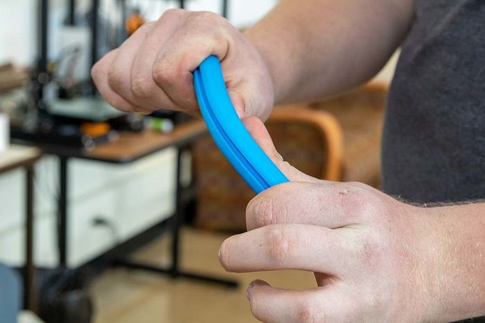 A blue 3d-printed tube is bent between Dan Foust's hands
