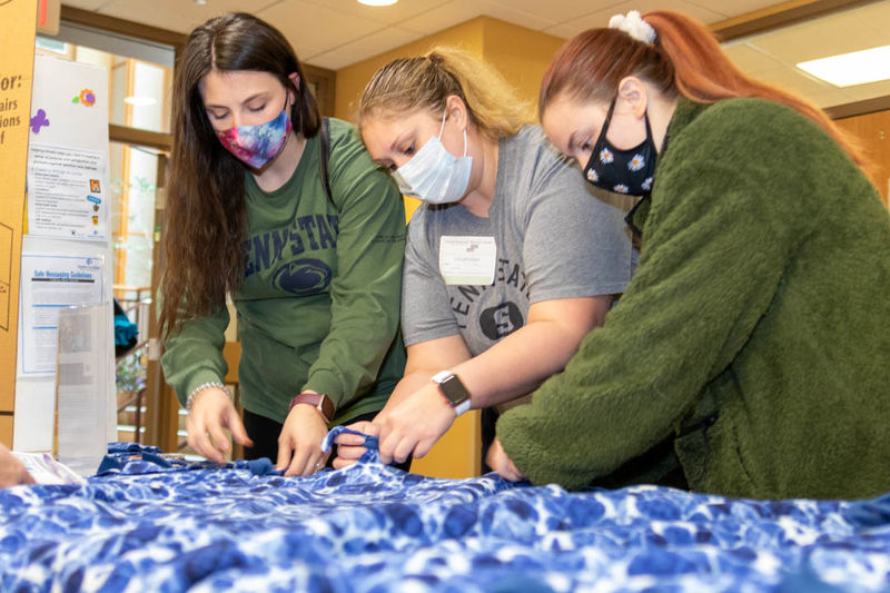 Three students knot ends of blanket