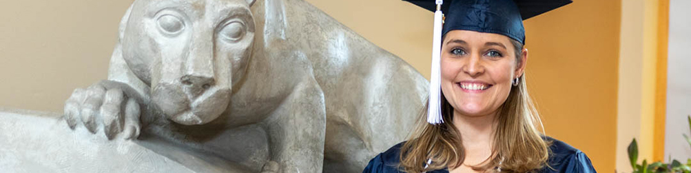 Student in graduation cap next to nittany lion shrine
