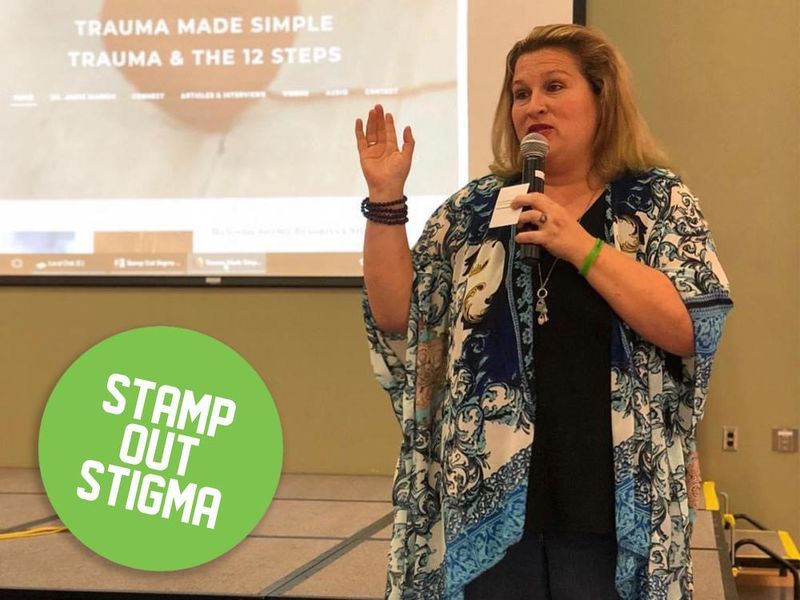 Jamie Marich holding a microphone and speaking with the Stamp Out Stigma logo overlayed