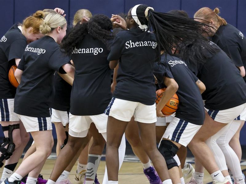 Group of women's basketball players wearing black shirts with white text saying Shenango are gathered on a court