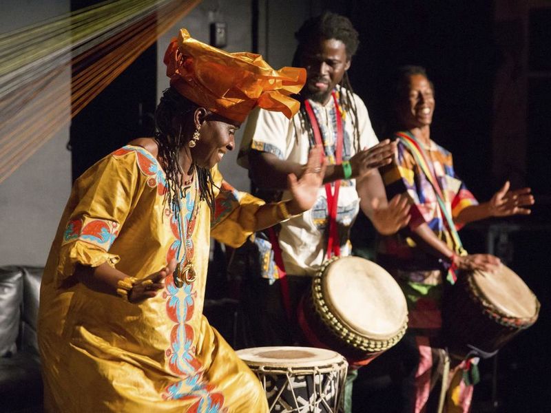 Dancer wearing traditional West African clothing performs with two drummers