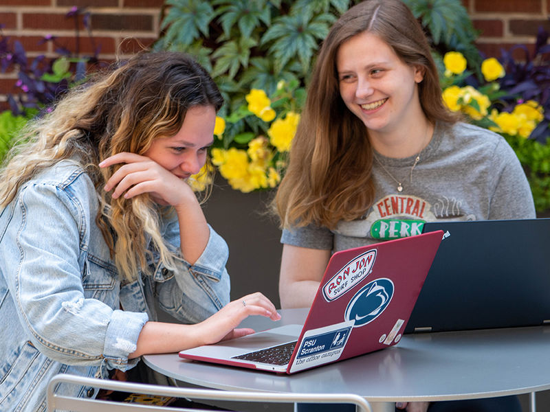 Two students working on laptops in outdoor courtyard