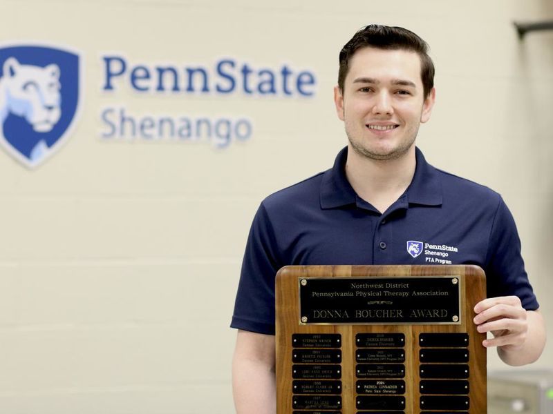 Patrick Connacher poses for a photo holding a plaque in front of a Penn State Shenango logo