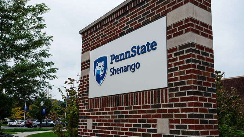 Brick entry sign that features the Penn State Shenango mark. Trees and a parking lot can be seen in the background. 