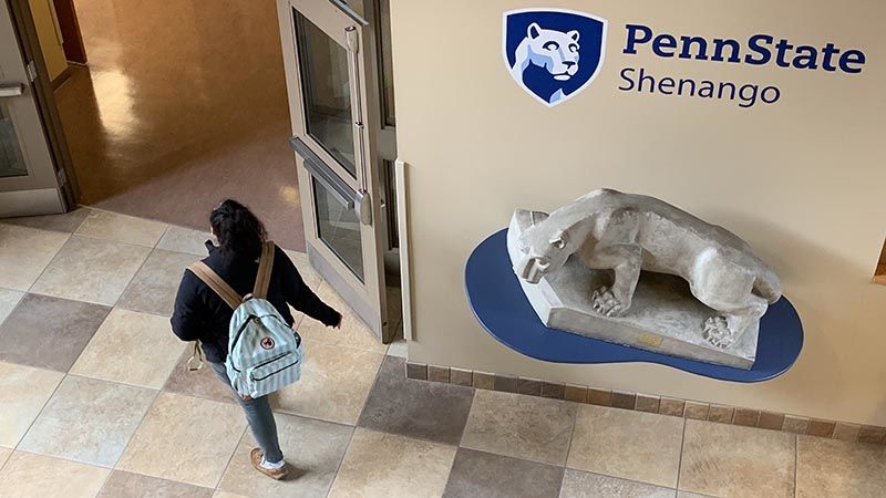 Student with backpack walks past small Lion Shrine 