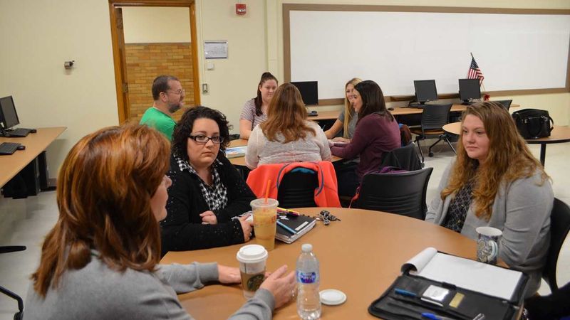 Students sitting around two round tables in a classroom discussing their project.