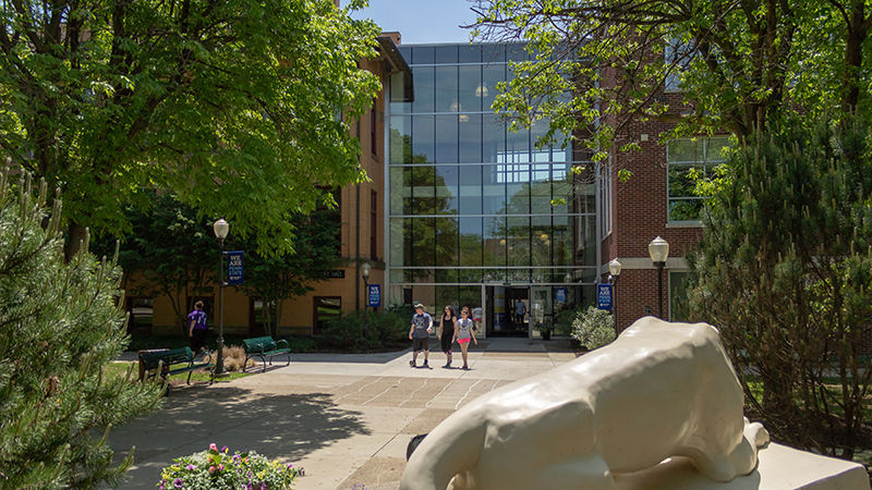 The back of the Lion Shrine is shown looking over the courtyard between Lecture and Sharon halls. Three students are walking through the courtyard. 