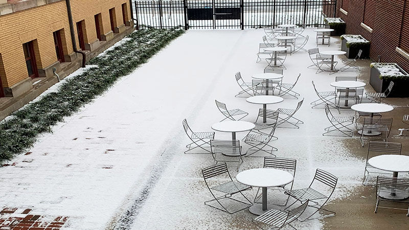 The table and ground of the courtyard are covered in a light dusting of snow. The courtyard is surrounded by Sharon Hall and Lecture Hall on either side. 