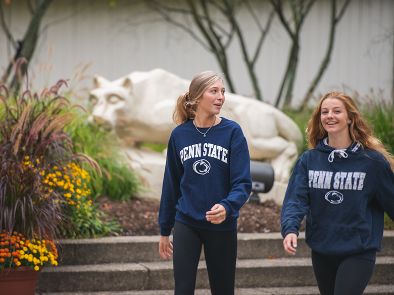 Two female students walking in front of the nittany lion shrine