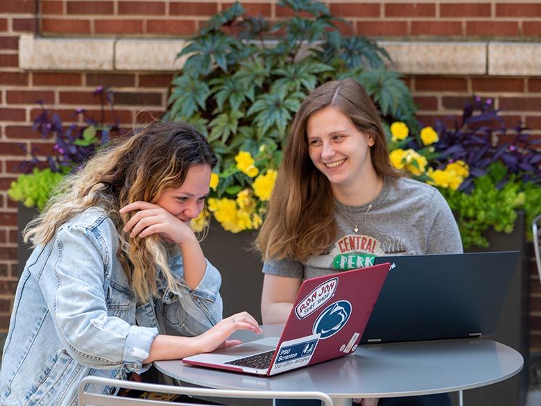 2 female students on laptops outside