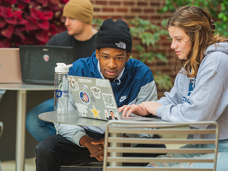 Two students studying on a computer outside at penn state shenango