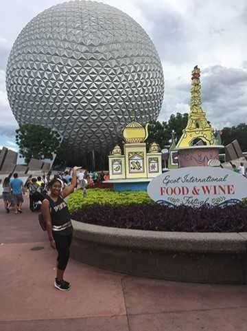 A young woman poses in the front entrance of Epcot in Disney World.