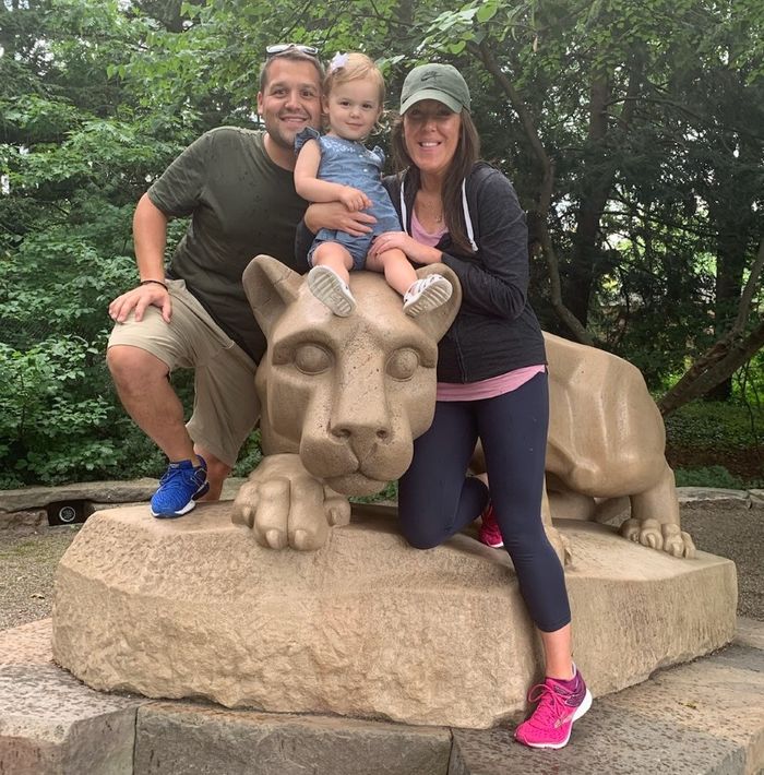 A man, his wife, and young daughter sitting on the Nittany Lion shrine.