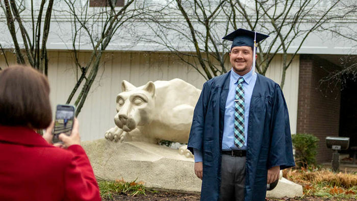 Student graduating with business marketing and management major has photo taken by Nittany Lion Shrine