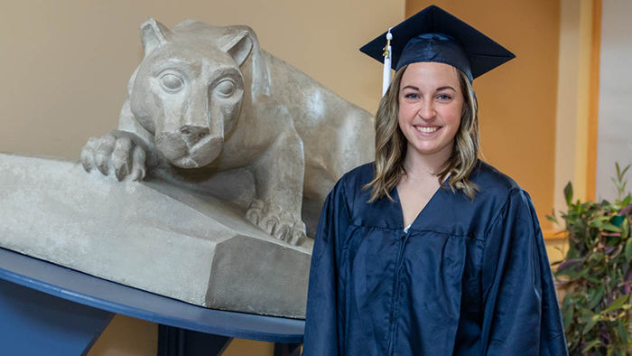 Occupational therapy student in graduation dress next to nittany lion shrine