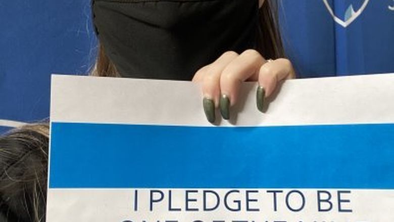Masked student holding sign that says "I pledge to be one of the nine"