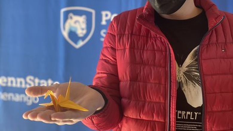 masked student holding an orange origami swan
