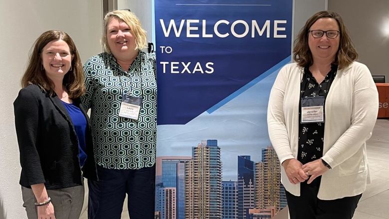 Three people pose next to a banner with text saying Welcome to Texas