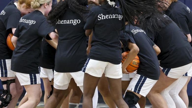 Group of women's basketball players wearing black shirts with white text saying Shenango are gathered on a court
