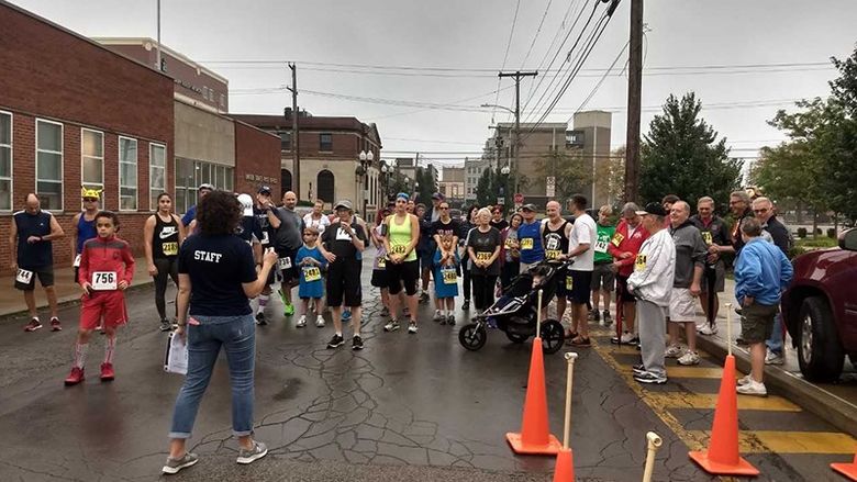 A group of people stand together on the street waiting to start to run or walk for a 5K race.