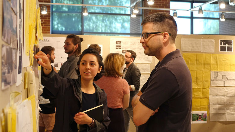 A female landscape architecture student points to her design during a critique by a landscape architecture faculty member.