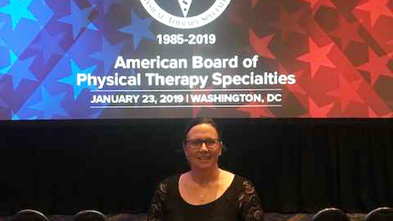 A woman standing in front of a projected image that reads recognition ceremony for clinical specialists celebrating clinical excellence 1985 to 2019 American Board of Physical Therapy Specialities January 23 2019 Washington DC