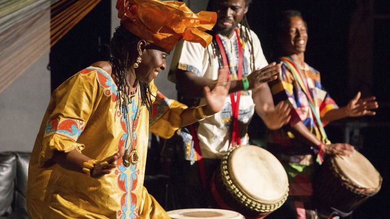 Dancer wearing traditional West African clothing performs with two drummers