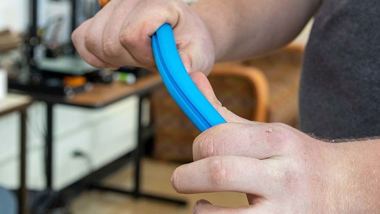 A blue 3d-printed tube is bent between Dan Foust's hands