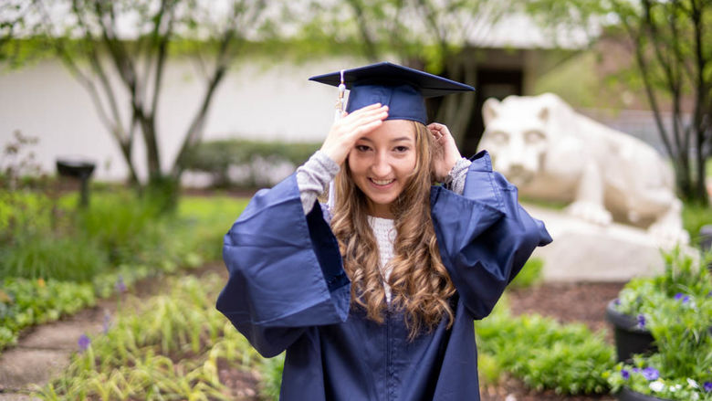 Kayleigh Miller fixing her graduation cap in front of the lion shrine