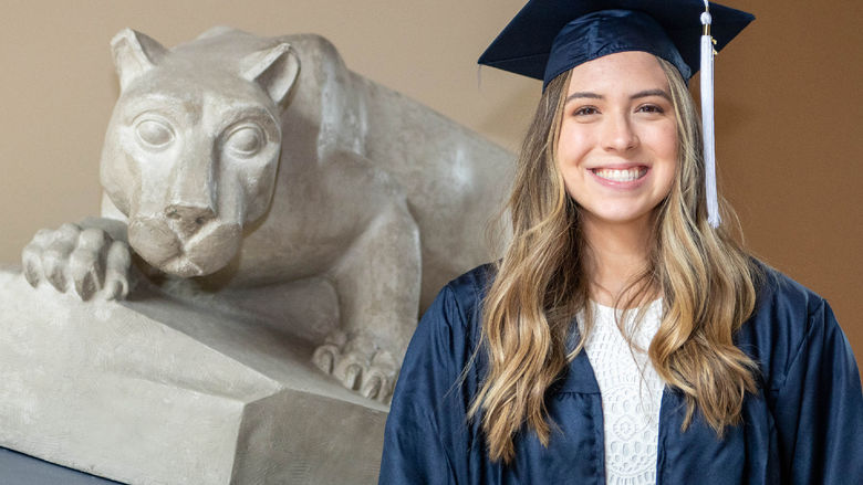 Rachel Maynard in cap and gown next to small Nittany Lion Shrine. 