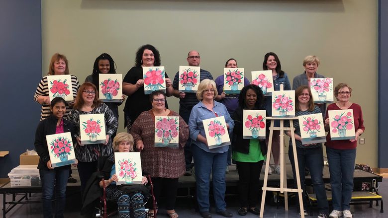 Group of people holding up individual paintings of flowers