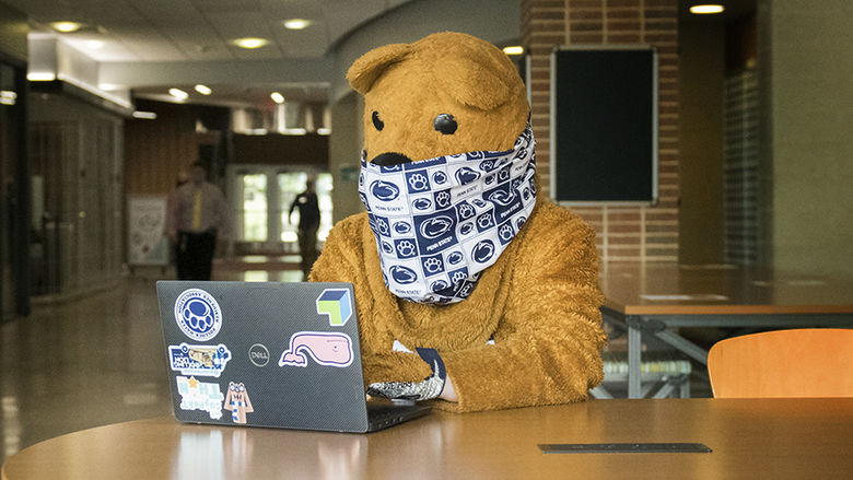 The Nittany Lion using a laptop while wearing a mask.