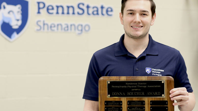 Patrick Connacher poses for a photo holding a plaque in front of a Penn State Shenango logo