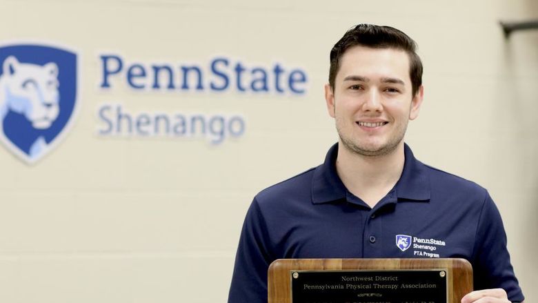 Patrick Connacher poses for a photo holding a plaque in front of a Penn State Shenango logo