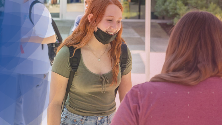 Female student outside talking with staff member at a table 