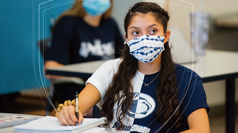 Female student taking notes while practicing social distancing and masking in a classroom. 