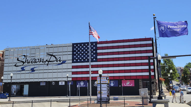 Exterior of a building with an American flag painted on the side and text saying Sharon, PA with sidewalks and flag poles in the foreground