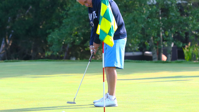 Golfer hits a golf ball towards a hole with a flag