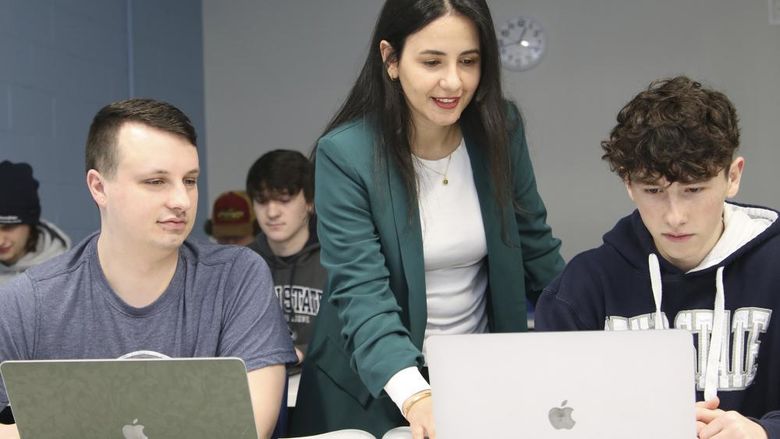 Professor Dima Rabadi works with students on laptops