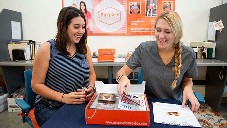 The two business owners of Purpose back the orange box with cards, frames, and papers