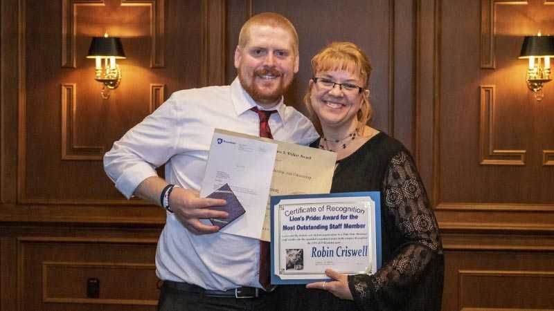 A young man and woman stand together with certificates in hand.