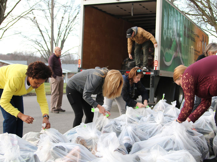 Group of people tagging large plastic bags full of shoes and loading them into a box truck