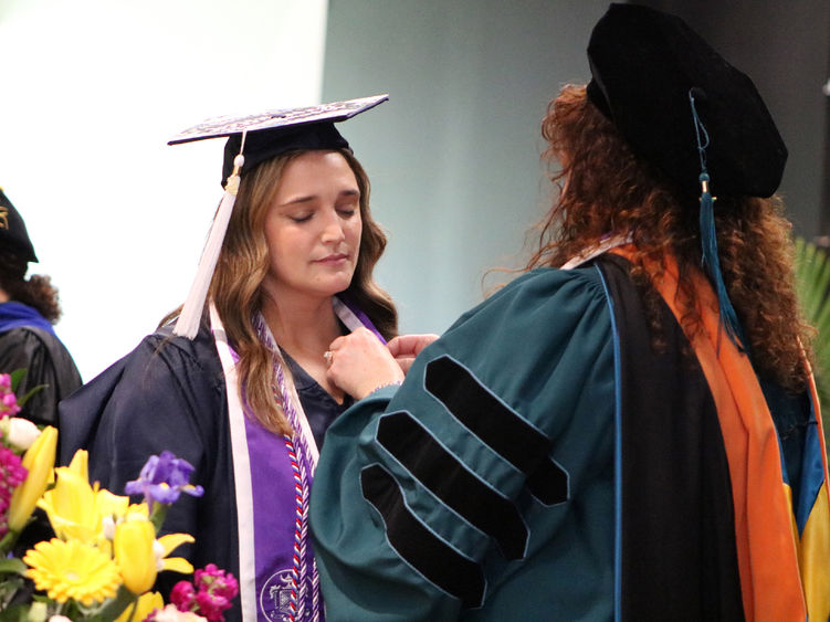 Faculty members adds pin to graduates lapel