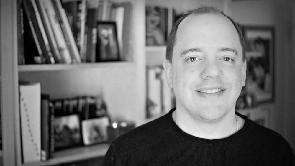 Photo of Brad Ricca in front of a book case.