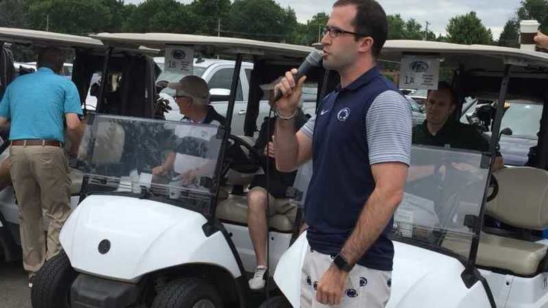 A man standing by a golf cart talking with a microphone.