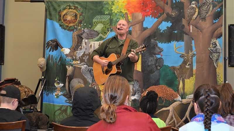 A musician plays his guitar on the stage in front of a colorful background.